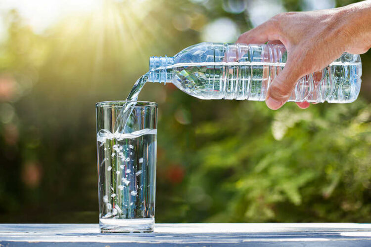 Hand, die aus einer Flasche Wasser in ein Glas gießt