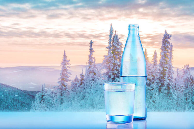 Wasserflasche und Glas vor winterlicher Gebirgslandschaft