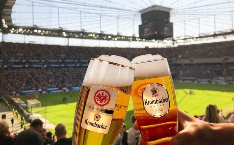 Zwei Krombacher Gläser vor Stadion-Hintergrund
