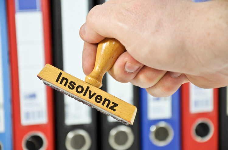Hand mit Stempel "Insolvenz" vor Aktenordnern