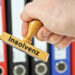 Hand mit Stempel "Insolvenz" vor Aktenordnern