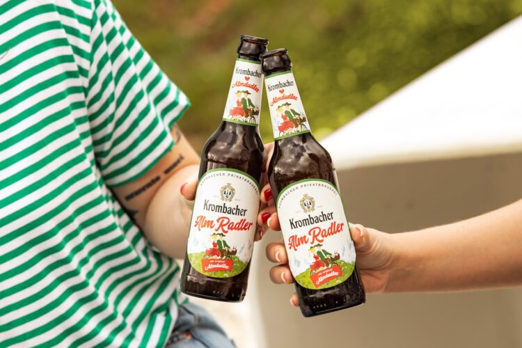 Zwei Hände stoßen mit Krombacher Almradler an.