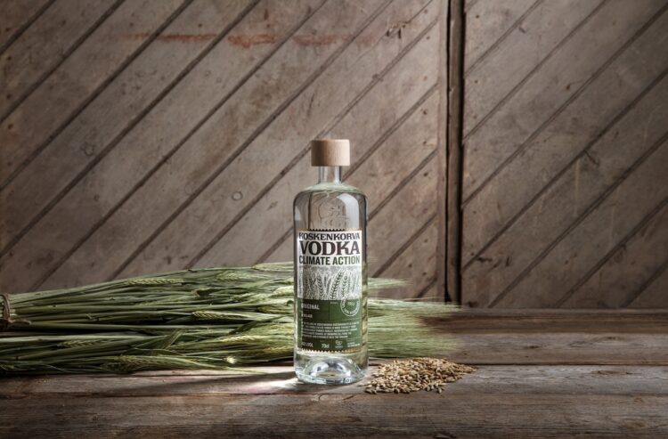 Koskenkorva-Flasche mit Getreide-Ähren vor Holzwand