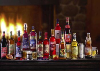 verschiedene Apfel- und Fruchtglühweine auf einem Tisch dekoriert mit Kaminfeuer im Hintergrund