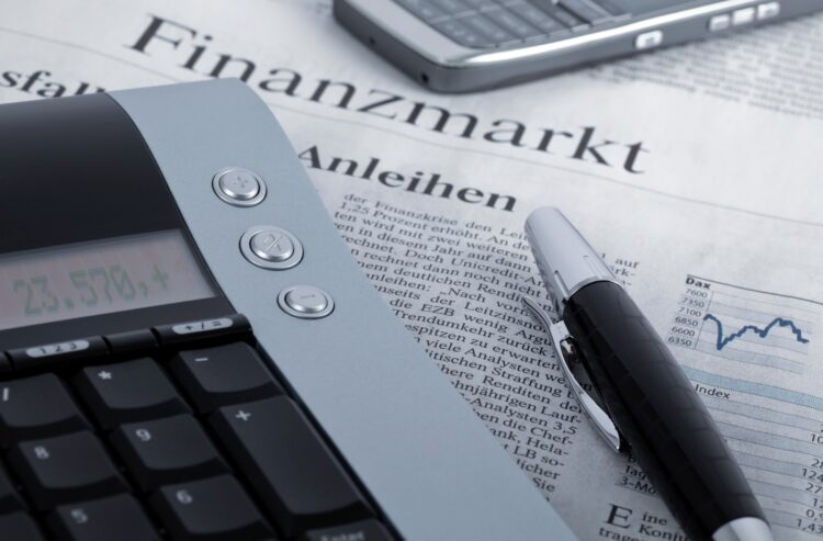 Taschenrechner, Stift und Smartphone auf dem Wirtschaftsteil einer Tageszeitung