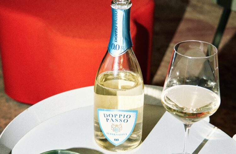 Die Alternativa Sparkling 0,0% von Doppio Passo und ein Glas auf einem kleinen Tisch