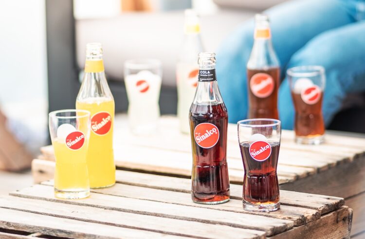 Flaschen und Gläser mit Sinalco-Limo und -Cola auf einem Holztisch