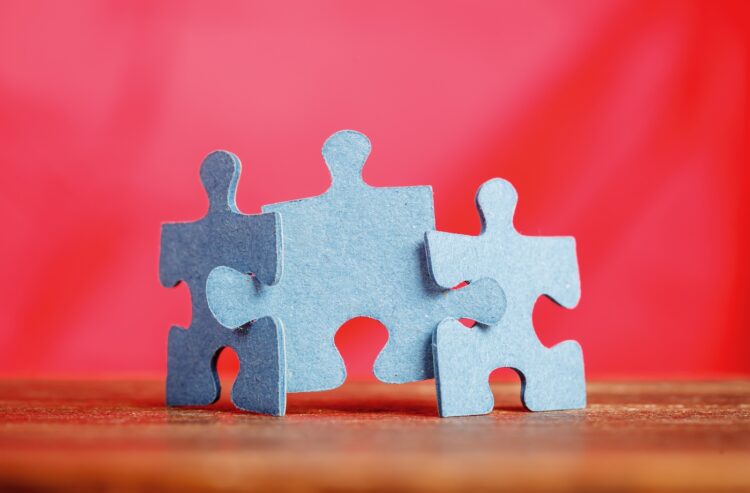 Drei Puzzleteile auf einem Tisch vor rotem Hintergrund